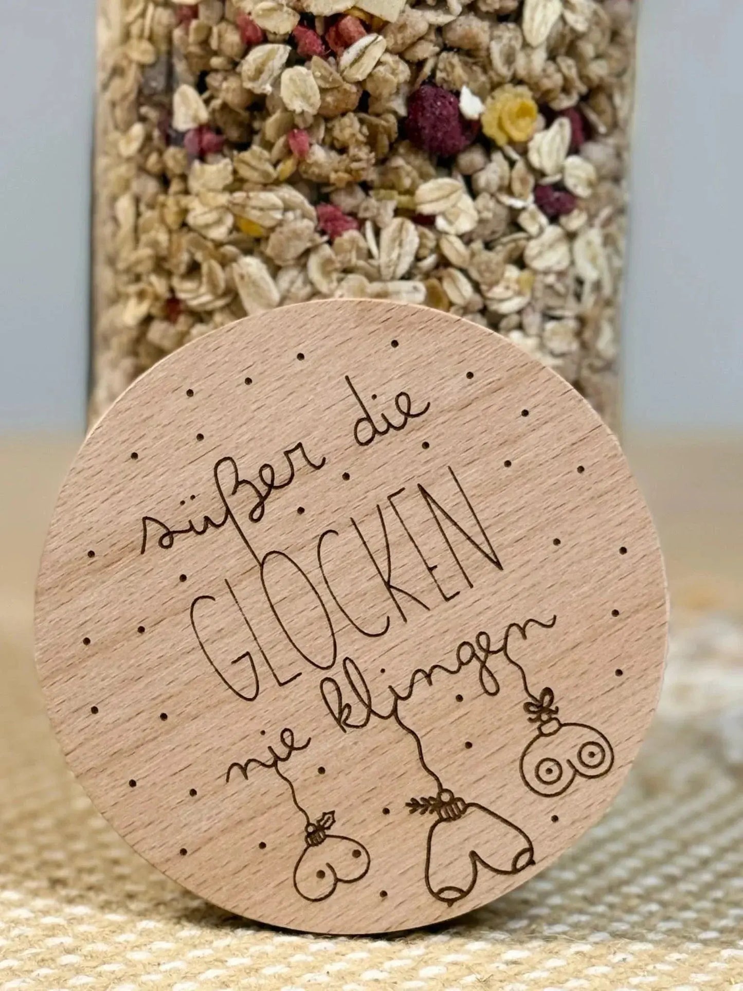 Runder Holzdeckel mit Gravur 'Süßer die Glocken nie klingen' und lustigen Motiven, vor Müsliglas.