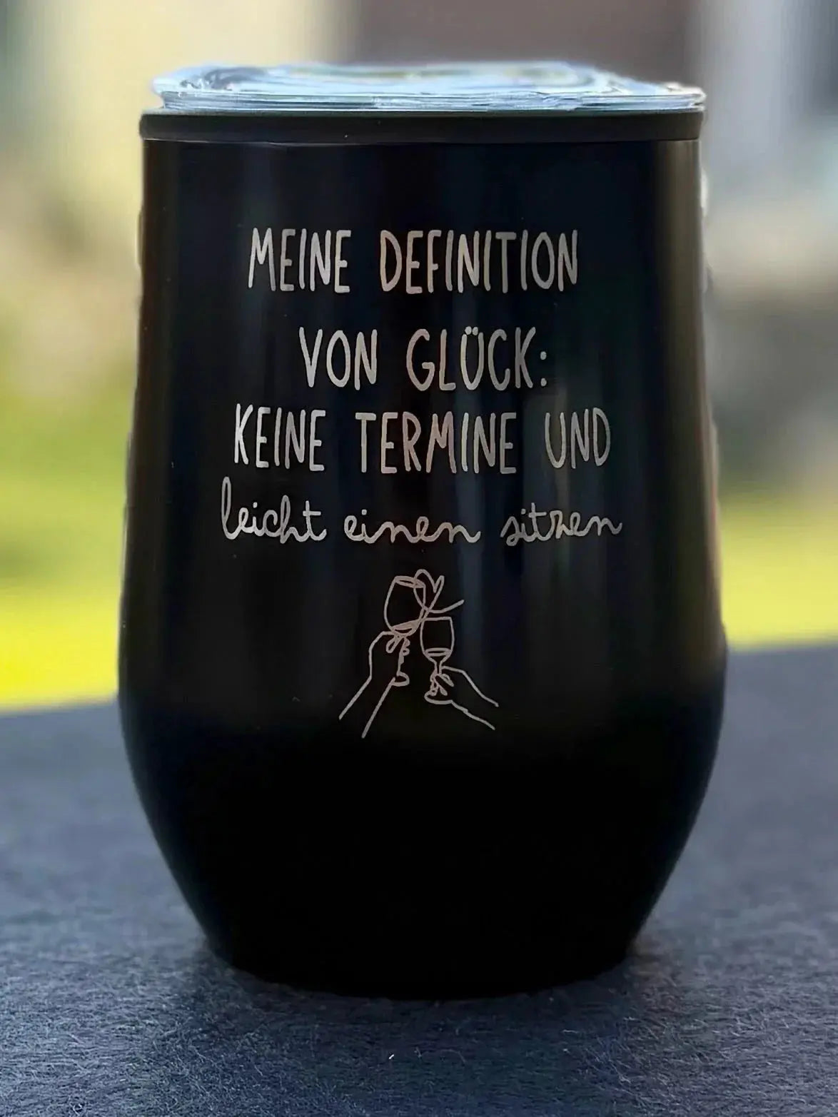 Schwarzer Becher mit Gravur 'Meine Definition von Glück' und Zeichnung zweier anstoßender Gläser, personalisiertes Geschenk von Lieblingsschuppen.de.