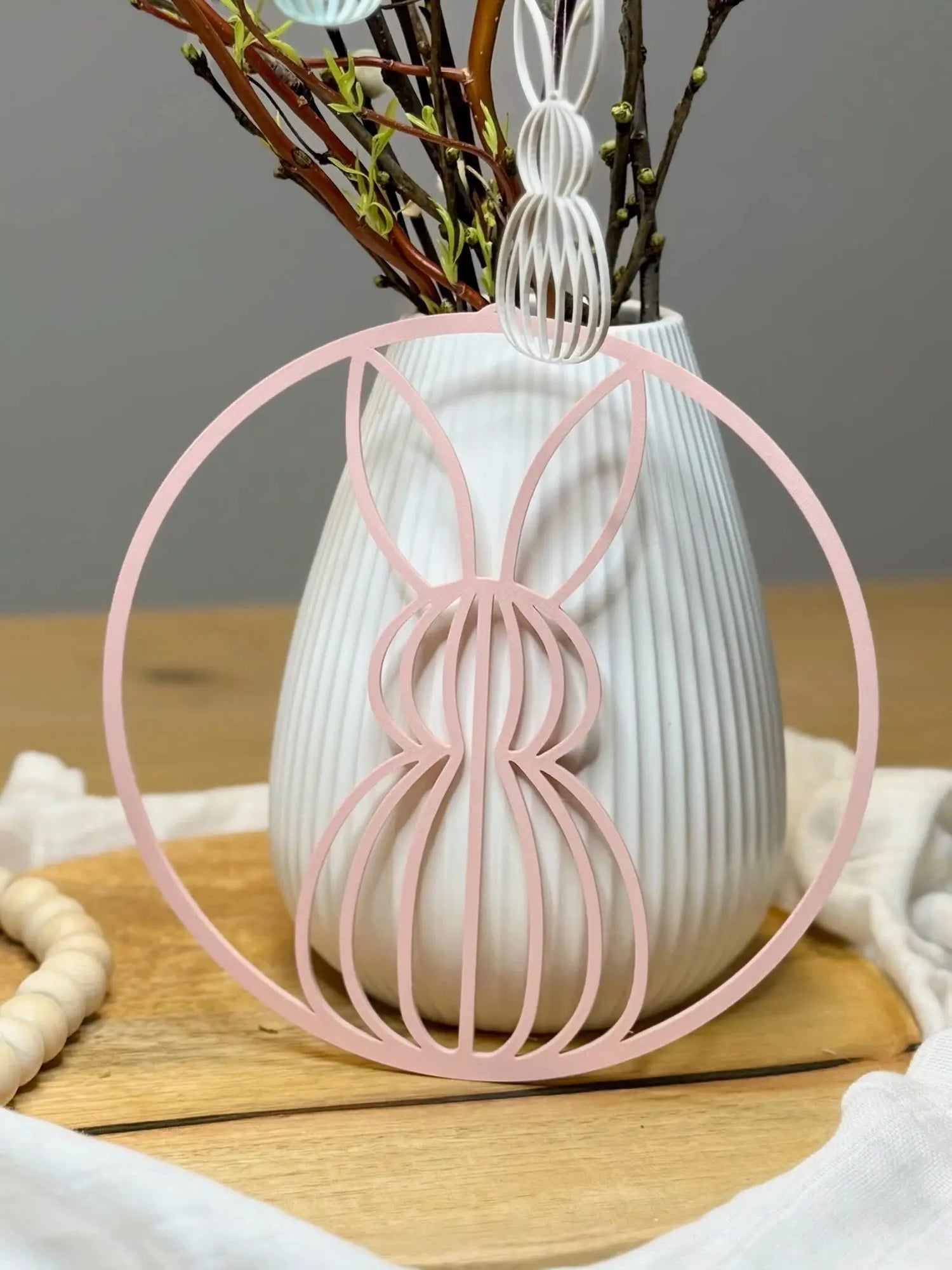 Osterdekoration Hase aus Holz in Rosa vor weißer Vase mit Zweigen auf Holztisch, Lieblingsschuppen.de