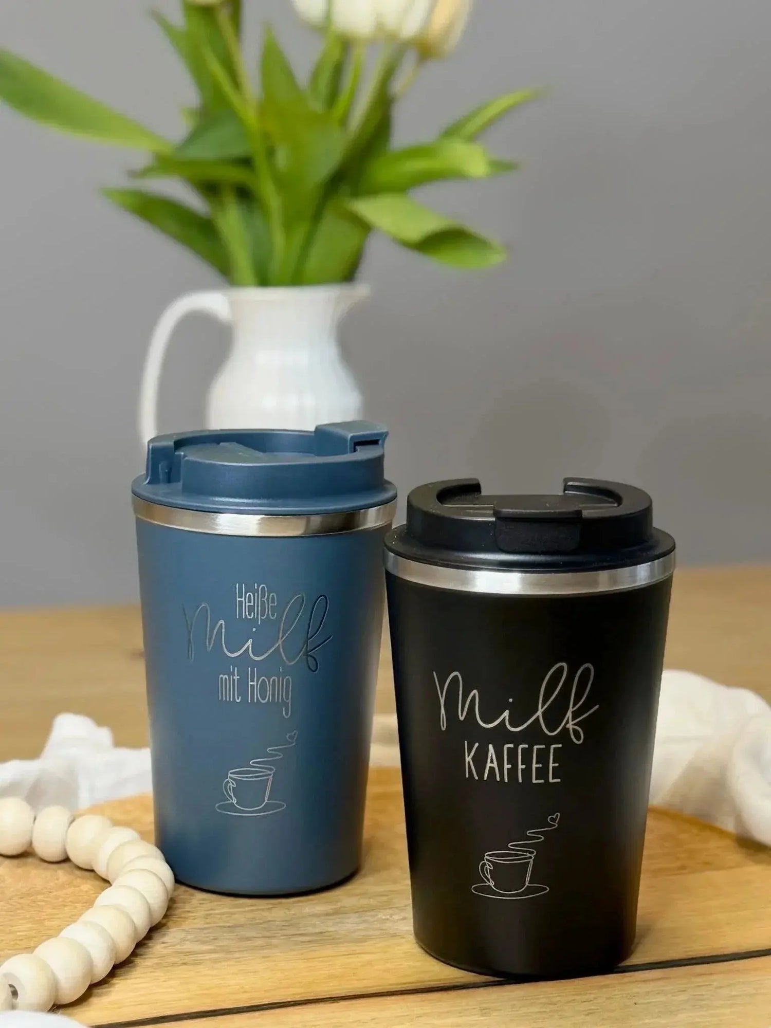 Zwei personalisierte Thermobecher mit Gravur, auf Holztisch vor Vase mit Tulpen, Lieblingsschuppen.de